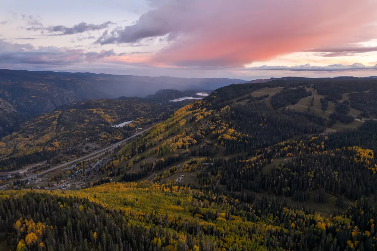 A panoramic view of rolling mountains adorned with autumn foliage under a vast, cloud-strewn sky. The scene invites viewers to imagine hiking and exploring the tranquil wilderness just beyond the resort.
