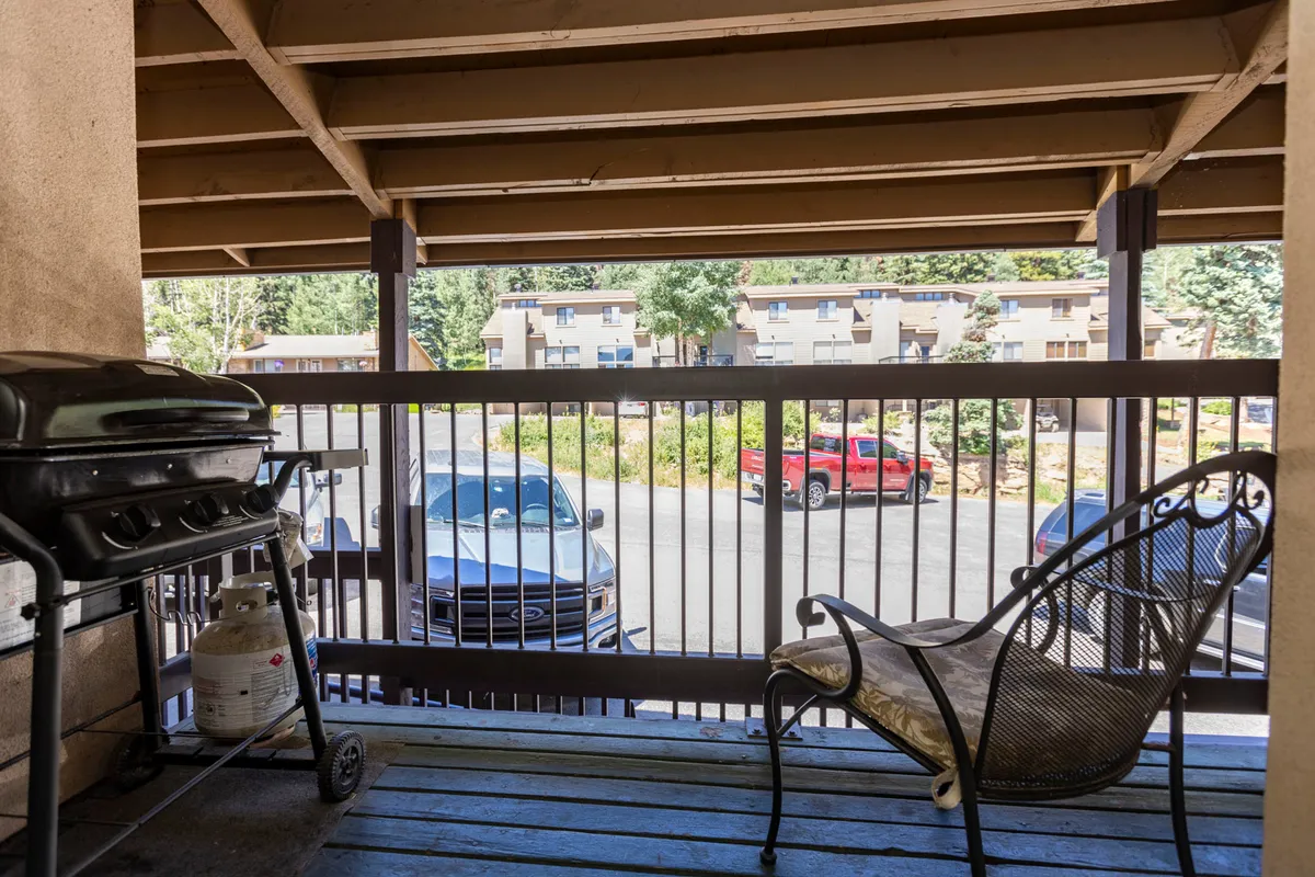 An inviting outdoor patio area featuring a grill, comfortable seating, and views of lush nature. The sunny setting suggests opportunities for relaxed gatherings or quiet mornings with coffee, surrounded by fresh mountain air.