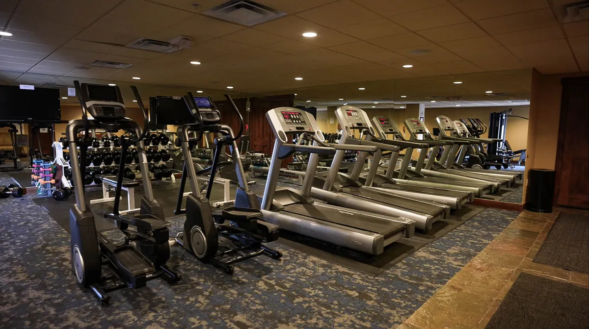 A bright and modern fitness center with treadmills, ellipticals, free weights, and mirrored walls, all neatly arranged. The space is clean and inviting, designed for both private and community fitness activities.