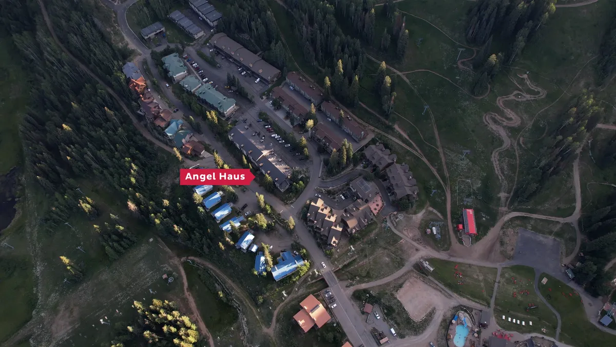 An expansive view of the Angel Haus building with the resort village and tree-lined surroundings. Roadways link to other buildings, hinting at the property's proximity to amenities and activities like skiing and hiking.