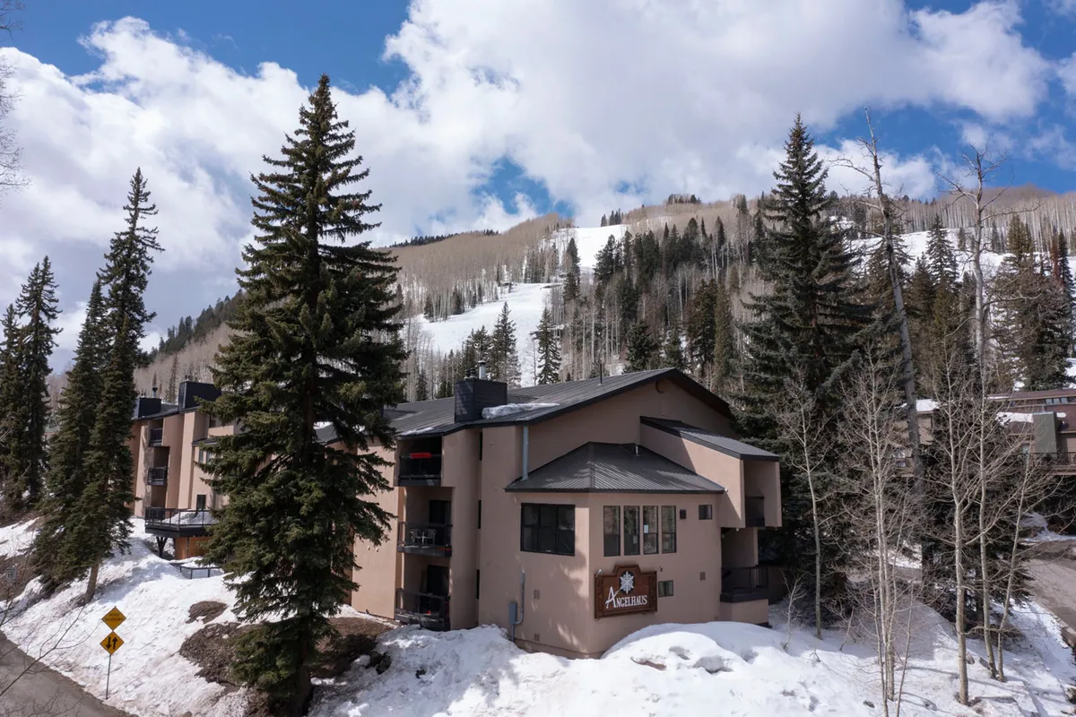 A peaceful exterior view featuring snow-covered ground, a wooded mountain backdrop, and the soft glow of sunset. The tranquil scene invites visitors to imagine winter adventures like skiing or snowboarding, as well as the calm that follows a day of exploration.