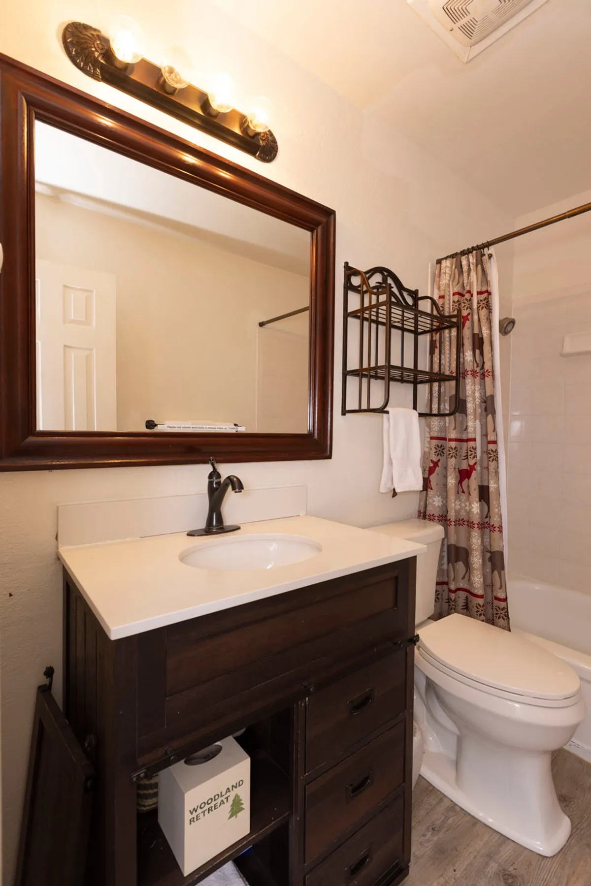 A cozy, softly lit interior bathroom scene featuring a wooden vanity, mirror, and shower curtain. The atmosphere suggests a relaxing and private environment suitable for pre-bed routines or peaceful mornings, with warm tones and thoughtful personal touches.